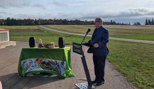 A man standing at a podium near a large green field.